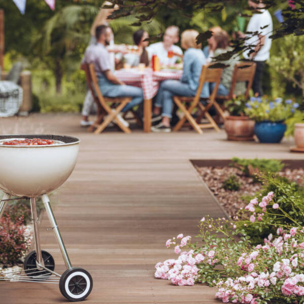 Grill with sausages in the garden with flowers and group of friends celebrating in the background